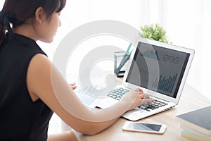 Beautiful young asian woman working and typing with laptop computer at office, businesswoman looking graph diagram analysis statis