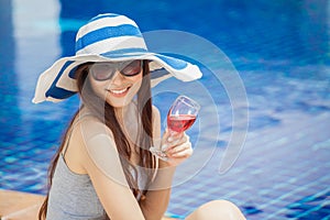 beautiful Young Asian women with beverages on summer party near the swimming pool .Happy girls in big hat and glasses relaxing