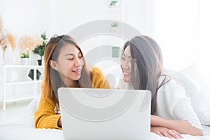 Beautiful young asian women LGBT lesbian happy couple sitting on bed hug and using laptop computer together bedroom at home.