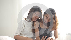 Beautiful young asian women LGBT lesbian happy couple sitting on bed hug and using phone together bedroom at home.