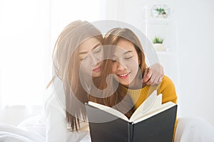 Beautiful young asian women LGBT lesbian happy couple sitting on bed reading book together near window in bedroom at home.