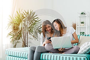 Beautiful young asian women LGBT lesbian happy couple sitting on sofa buying online using laptop a computer and phone in living.