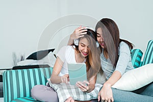 Beautiful young asian women LGBT lesbian happy couple sitting on sofa buying online using tablet in living room at home.