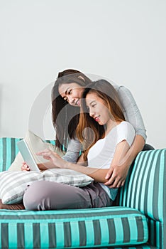 Beautiful young asian women LGBT lesbian happy couple sitting on sofa buying online using tablet in living room at home.