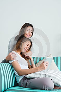 Beautiful young asian women LGBT lesbian happy couple sitting on sofa buying online using tablet in living room at home.