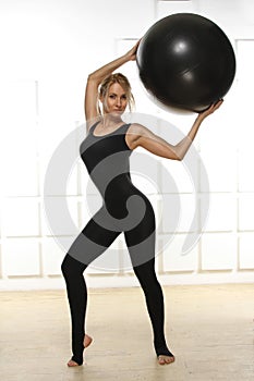 Beautiful young attractive beautiful woman with blond hair standing holding up ball for fitness black dressed up in black suit e