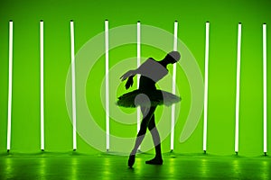 Beautiful young ballerina dancing classical ballet in a dark studio against a background of bright green neon lights