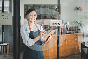 Beautiful young barista woman in apron holding order paper and standing in front of the door
