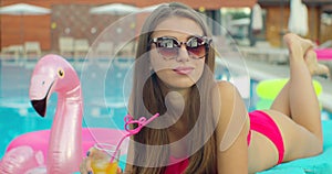 Beautiful young bikini woman in summer drinking a cocktail. Girl relaxing in tropical swimming pool. Portrait of young