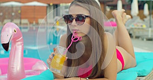 Beautiful young bikini woman in summer drinking a cocktail. Girl relaxing in tropical swimming pool. Portrait of young