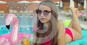 Beautiful young bikini woman in summer drinking a cocktail. Girl relaxing in tropical swimming pool. Portrait of young