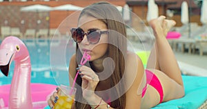 Beautiful young bikini woman in summer drinking a cocktail. Girl relaxing in tropical swimming pool. Portrait of young