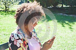 Beautiful young black woman laughing and looking at the smartphone at the park