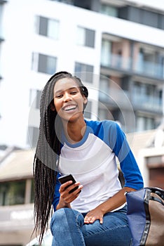 Beautiful young black woman sitting outdoors with cellphone and smiling