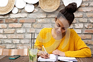 Beautiful young black woman writing notes at cafe