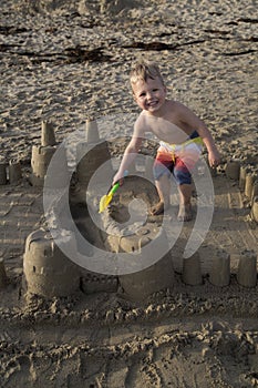 Beautiful young blond boy playing on beach in a sand castle