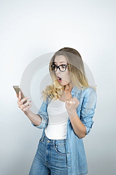 Beautiful young blond surprised woman holding smartphone looks happy close up  white background