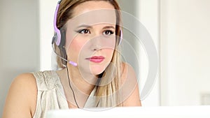 Beautiful young blond telesales woman with headphones on computer talking to customer over the phone