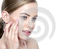 Beautiful Young Blond Woman applying Face cream under her eyes. Facial treatment. Cosmetology, beauty and spa concept