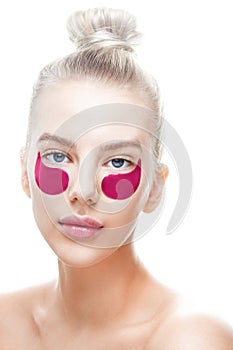Beautiful young blond woman with blue eyes and plump lips with pink eye patches on a white background isolated. Personal care, fac