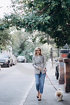 Beautiful young blond woman with her pet Pomeranian Spitz dog breed for a walk. Little fluffy dog. Soft selective focus