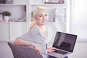 Beautiful young blond woman at home sitting on sofa or settee using her laptop computer