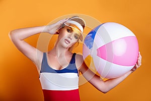 Beautiful young blond woman posing in swimsuit and yellow plastic visor with inflatable ball