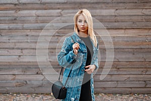Beautiful young blond woman with a stylish leather handbag in a fashionable denim jacket in a black dress