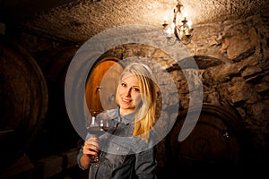 Beautiful young blond woman tasting red wine in a wine cellar