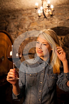 Beautiful young blond woman tasting red wine in a wine cellar