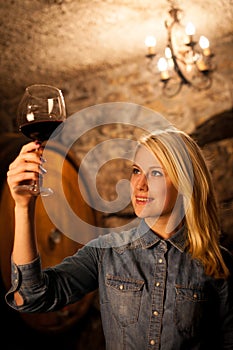 Beautiful young blond woman tasting red wine in a wine cellar