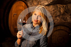 Beautiful young blond woman tasting red wine in a wine cellar