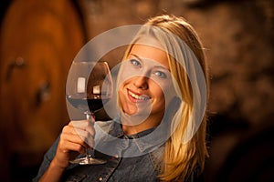 Beautiful young blond woman tasting red wine in a wine cellar