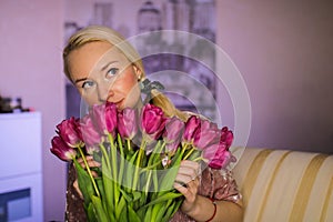 Beautiful young blond woman with tulip bouquet. Spring portrait. At home. Interior. Mother`s Day