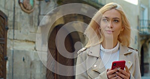 Beautiful young blond woman using phone in the old city center. Chatting with friends, girl using cellphone outdoors