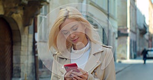 Beautiful young blond woman using phone in the old city center. Chatting with friends, girl using cellphone outdoors