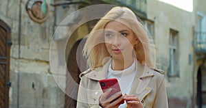 Beautiful young blond woman using phone in the old city center. Chatting with friends, girl using cellphone outdoors