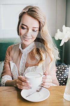 Beautiful young blond woman in a white dress enjoying coffee cappuccino with foam