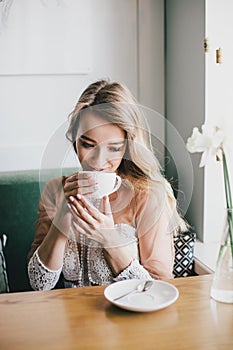 Beautiful young blond woman in a white dress enjoying coffee cappuccino with foam