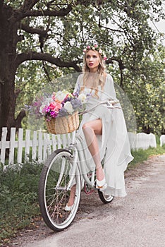 beautiful young blonde bride riding bicycle with flower