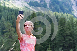 Beautiful young blonde Caucasian woman taking a selfie with smartphone outdoors in park