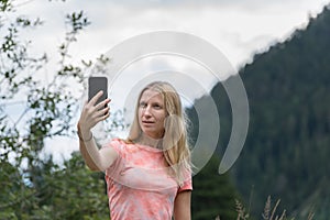 Beautiful young blonde Caucasian woman taking a selfie with smartphone outdoors in park