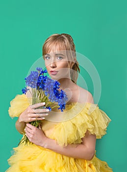 Beautiful young blonde caucasian woman in yellow dress with blue cornflower on green background.