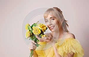 Beautiful young blonde caucasian woman in yellow dress with yellow roses.