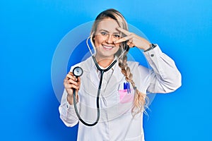 Beautiful young blonde doctor woman holding stethoscope doing peace symbol with fingers over face, smiling cheerful showing