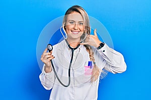 Beautiful young blonde doctor woman holding stethoscope smiling doing phone gesture with hand and fingers like talking on the