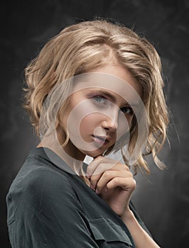 Beautiful young blonde girl with disheveled hairstyle and nude makeup, wearing a shirt and jeans emotionally posing on a gray