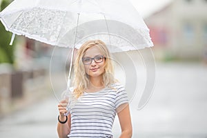 Beautiful young blonde girl holding umbrella in summer rain