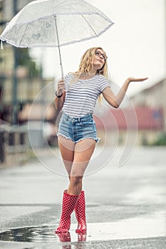 Beautiful young blonde girl holding umbrella in summer rain