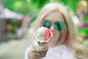 Beautiful, young blonde girl with ice cream in her hands, licks the ice cream on the background of a green park. Italian ice cream